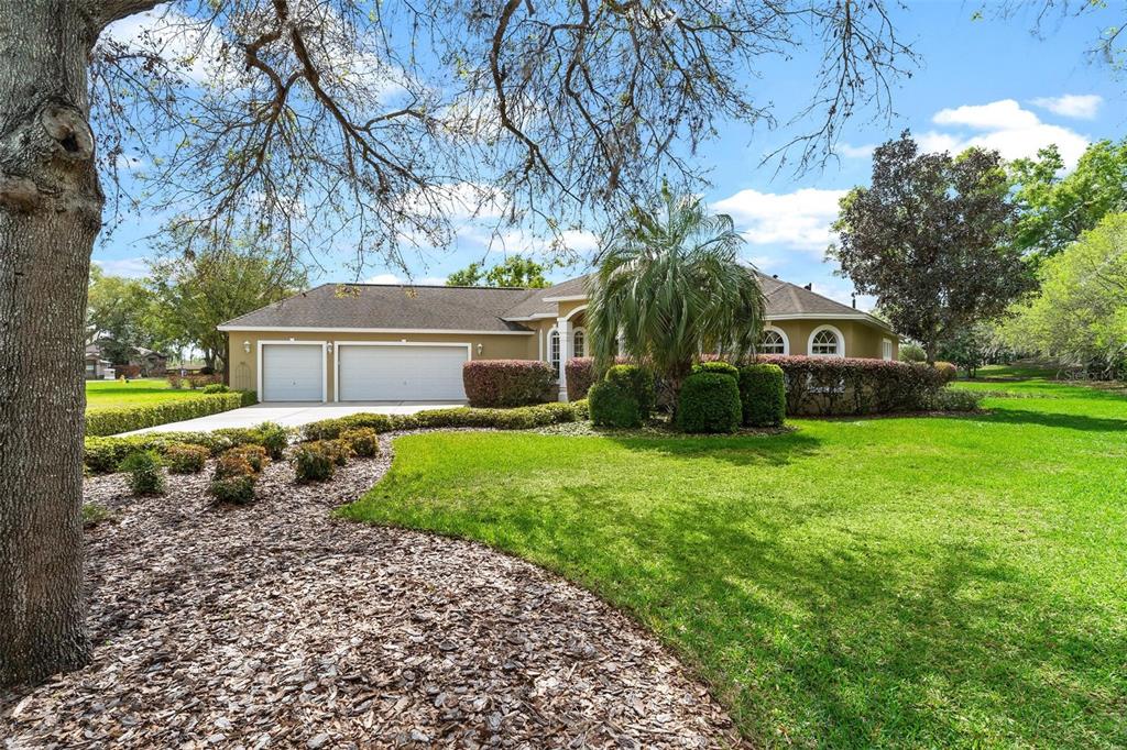 A single-story house with a two-car garage, a large lawn, and mature landscaping — 6053 SPINNAKER LOOP, LADY LAKE, FL