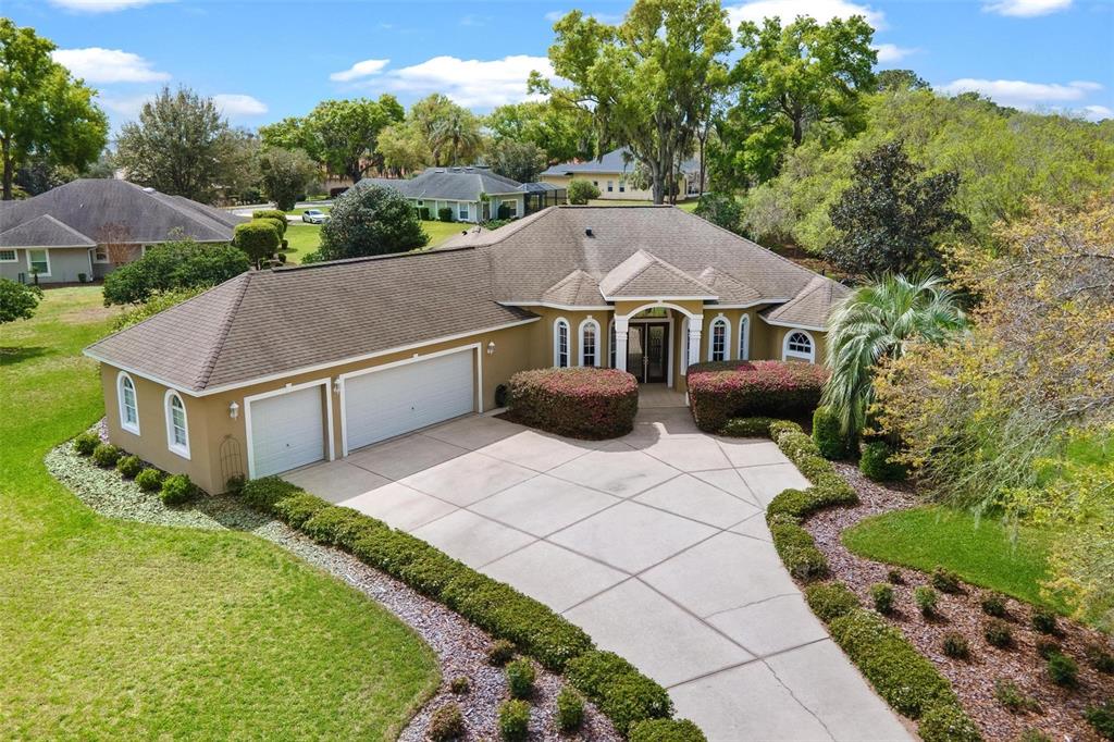 An aerial view of a tan, single-story house with a three-car garage and driveway — 6053 SPINNAKER LOOP, LADY LAKE, FL