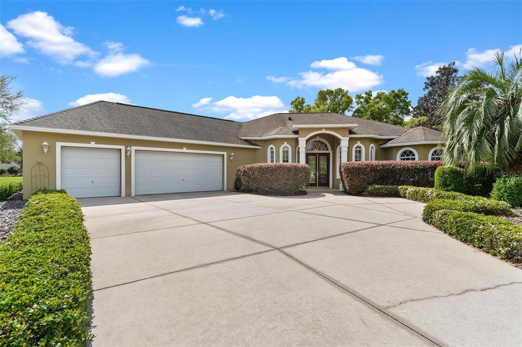 A single-story house with a three-car garage, arched entryway, and a large concrete driveway — 6053 SPINNAKER LOOP, LADY LAKE, FL