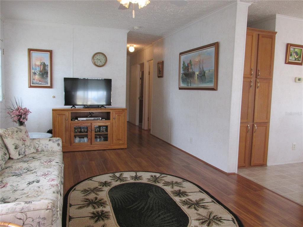 A living room features wood-look flooring, a floral sofa, a television console, and wall art — 5 QUEEN OF WATERS STREET, LAKE WALES, FL
