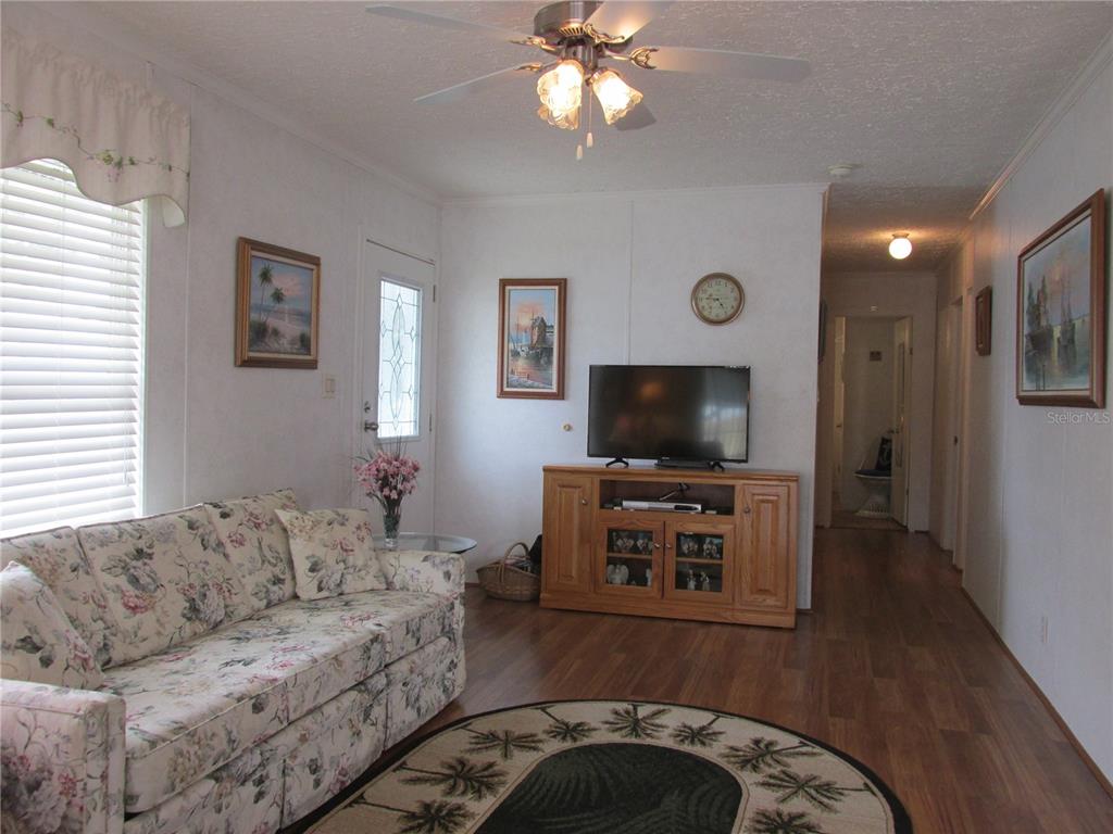 A living room features a floral sofa, wood-look flooring, a ceiling fan, and a television console — 5 QUEEN OF WATERS STREET, LAKE WALES, FL