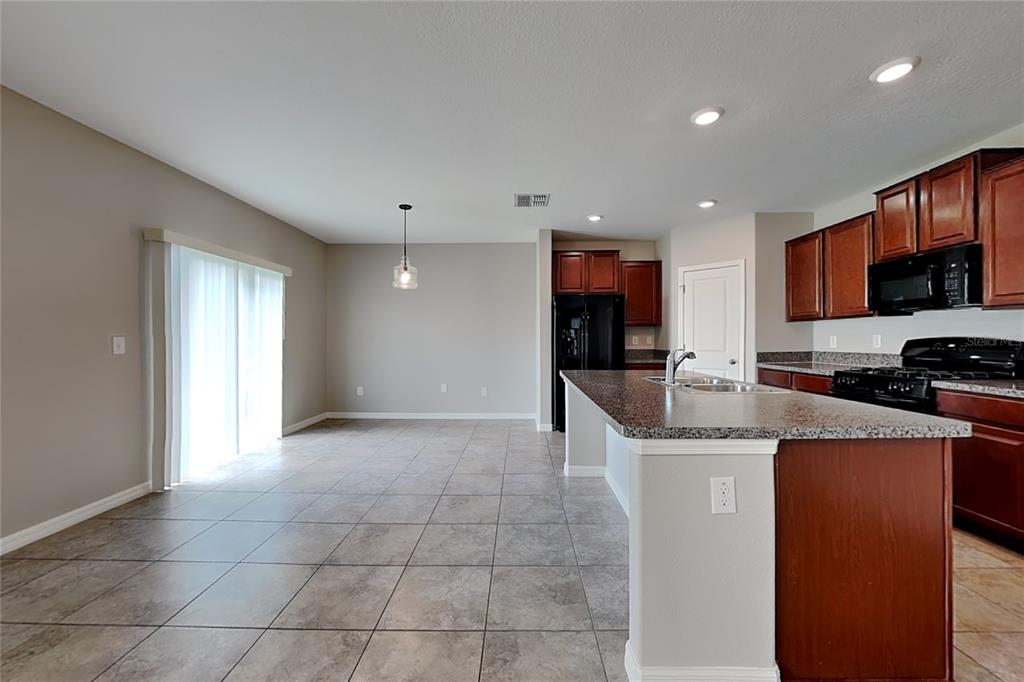 A kitchen with dark wood cabinets, granite countertops, and tile flooring opens to a dining area — 4906 WHITE CHICORY DRIVE, APOLLO BEACH, FL