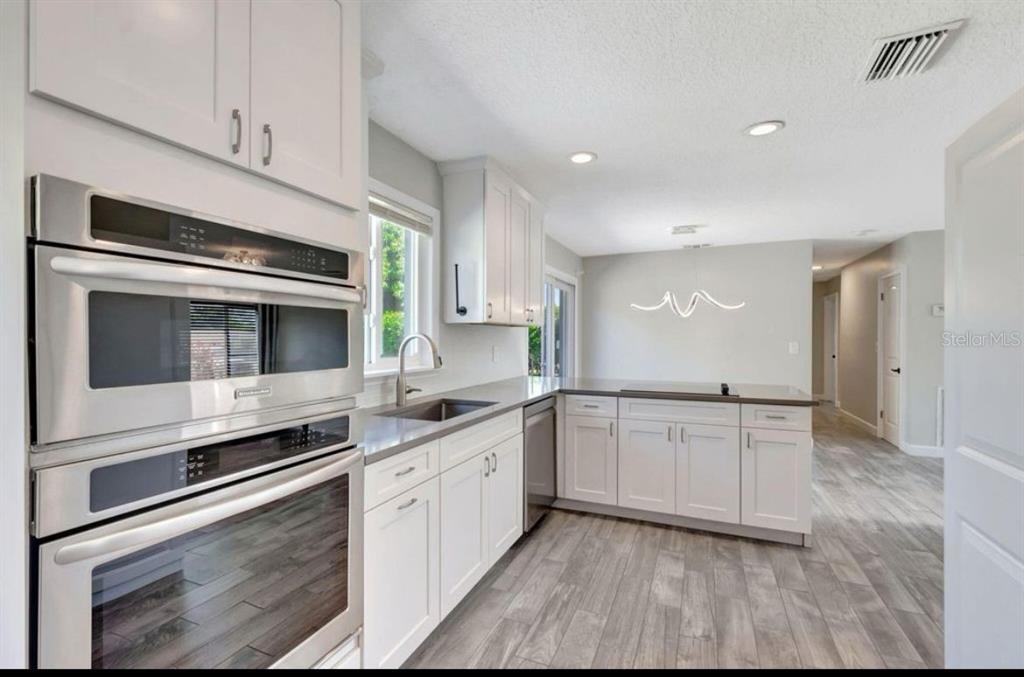 A modern kitchen features white cabinetry, stainless steel appliances, gray countertops, and wood-look tile flooring — 125 SE 6TH AVENUE, BOYNTON BEACH, FL