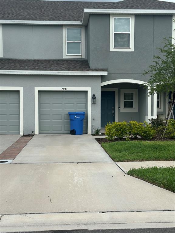 A gray two-story townhouse features a single-car garage, a blue trash bin, and a front entrance — 2358 PARAVANE WAY, WESLEY CHAPEL, FL