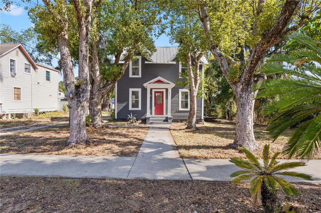 A two-story gray house with a red front door sits behind large trees — 821 E LEMON AVENUE, EUSTIS, FL
