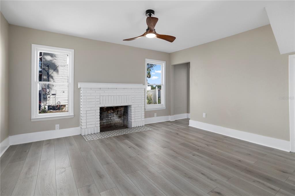 A living room features light gray wood-look flooring, a white brick fireplace, and a ceiling fan — 821 E LEMON AVENUE, EUSTIS, FL