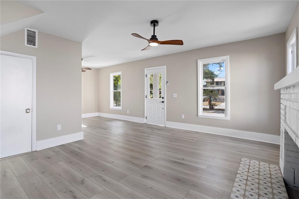 A living room with light wood-look flooring, a ceiling fan, and a white brick fireplace — 821 E LEMON AVENUE, EUSTIS, FL