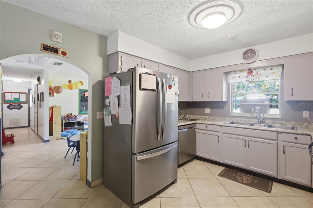 A kitchen with light gray cabinets, stainless steel appliances, and tile flooring leads to a classroom — 601 N PEACH STREET, BUNNELL, FL