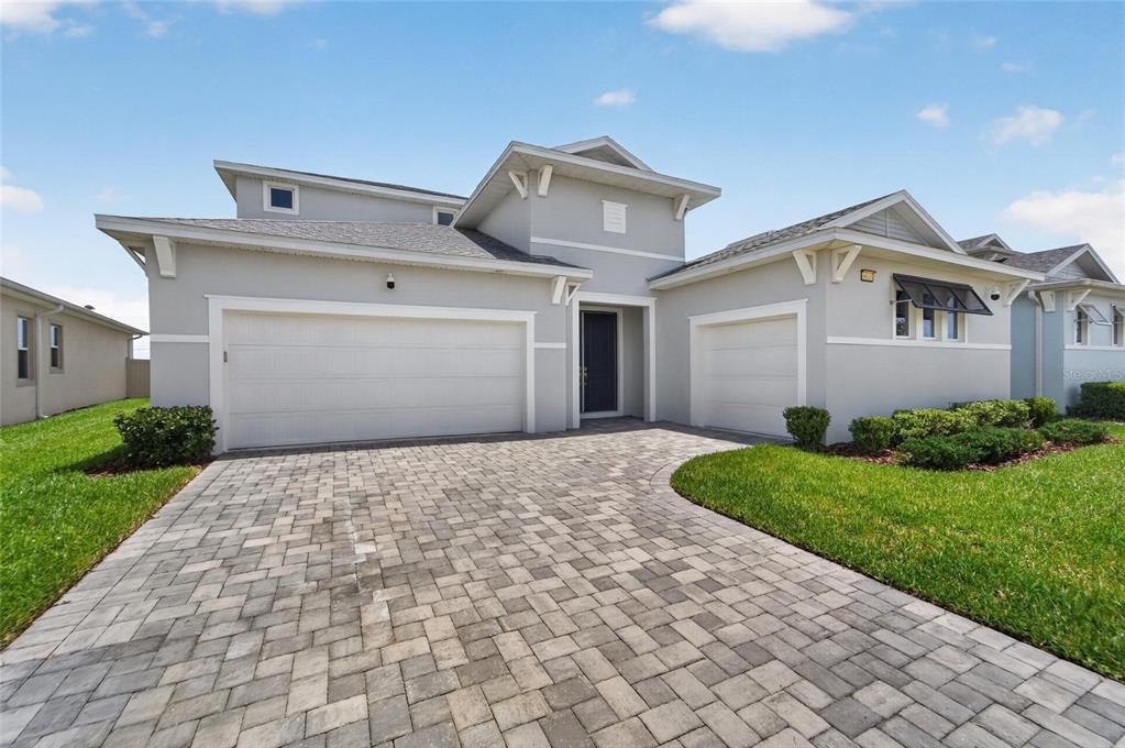 A two-story house with a gray exterior, a paver driveway, and two garage doors — 8910 DRUMMER PLANK DRIVE, WESLEY CHAPEL, FL