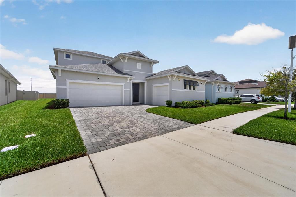 A gray two-story house features a paver driveway, a two-car garage, and a green lawn — 8910 DRUMMER PLANK DRIVE, WESLEY CHAPEL, FL