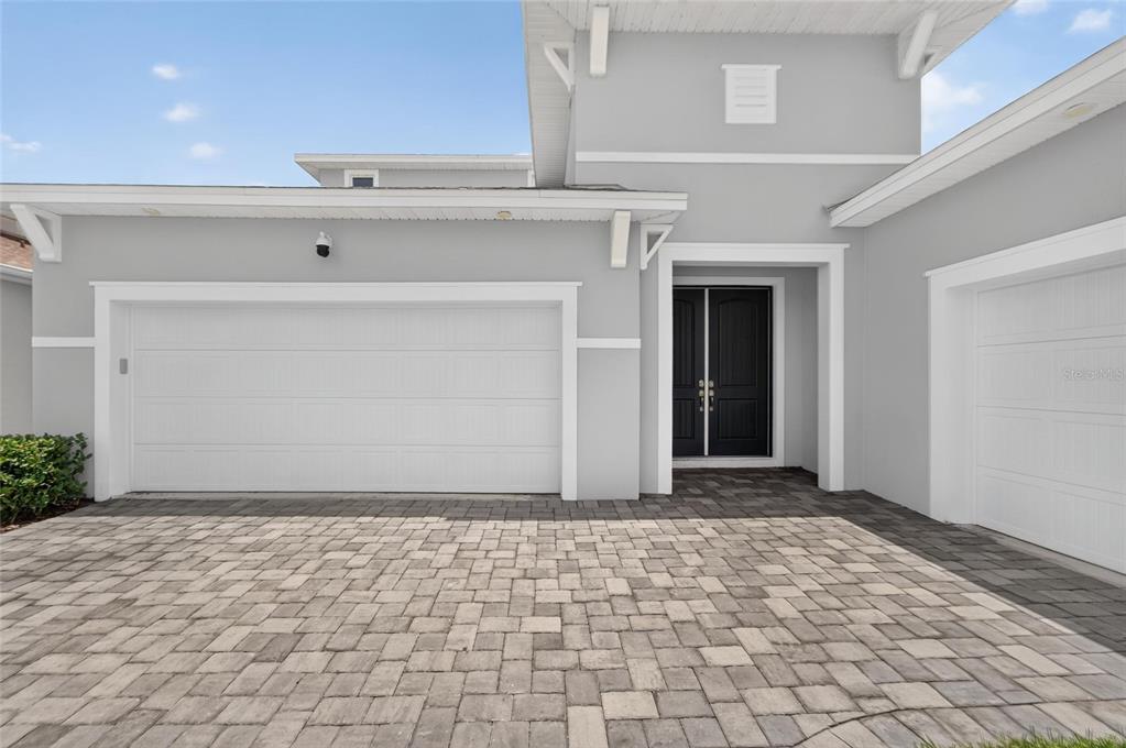 A gray house exterior features a double garage, a dark front door, and paver driveway — 8910 DRUMMER PLANK DRIVE, WESLEY CHAPEL, FL