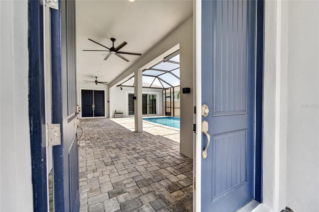 A view through an open blue door reveals a covered patio with a swimming pool — 8910 DRUMMER PLANK DRIVE, WESLEY CHAPEL, FL