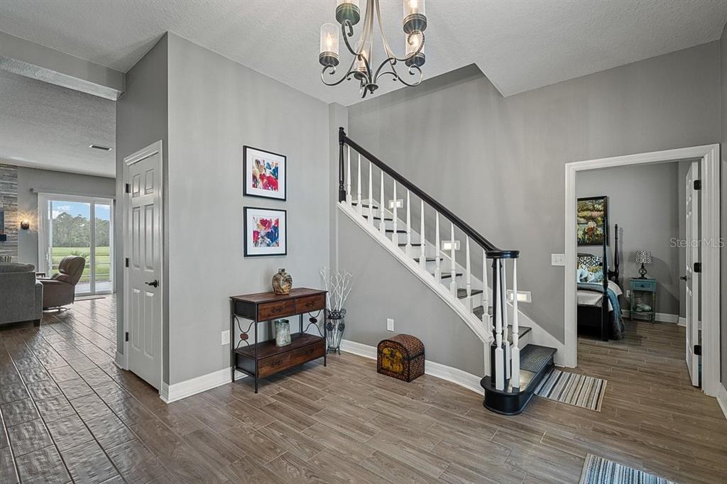 An entryway features wood-look tile flooring, a staircase with a dark railing, and a chandelier — 92 LAGARE STREET, PALM COAST, FL
