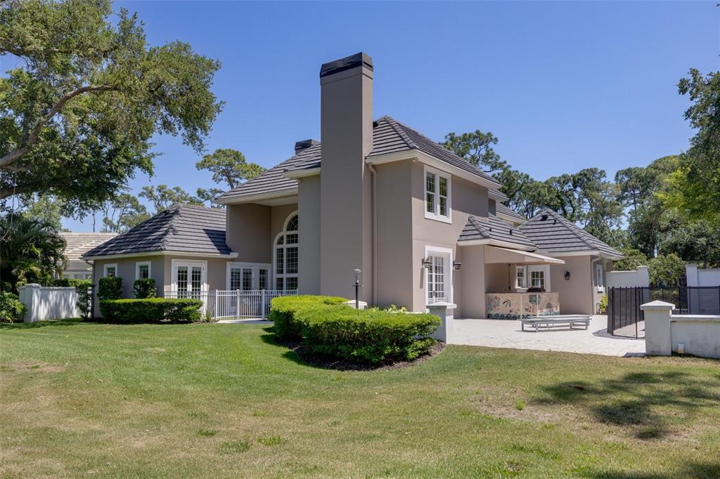 The exterior of a two-story house features a large chimney, tiled roof, and patio area — 97 SUGAR MILL DRIVE, OSPREY, FL
