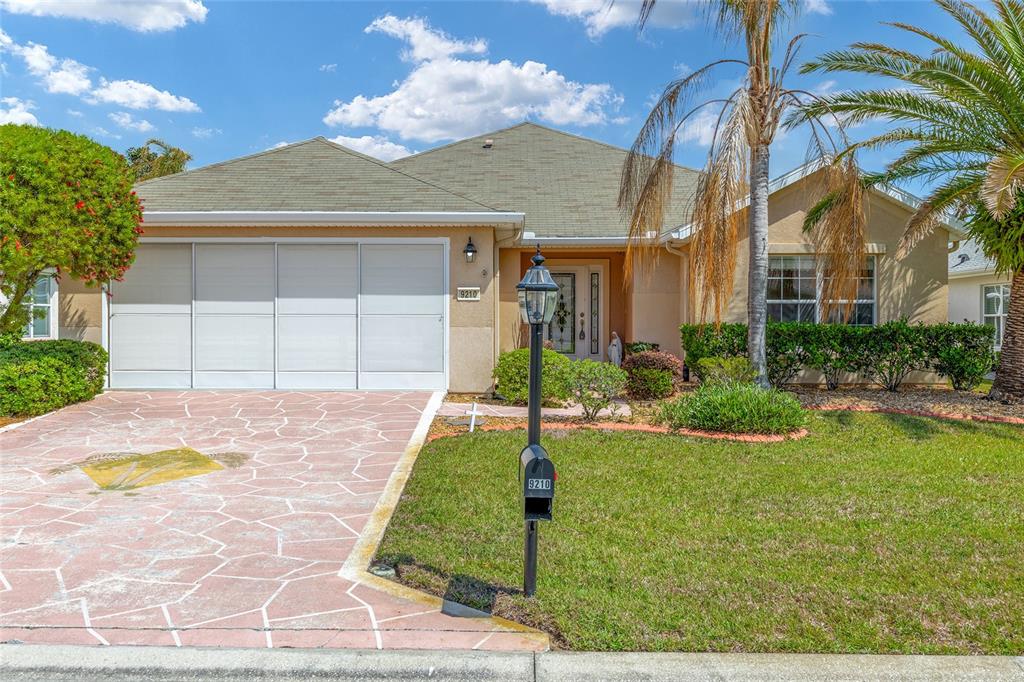 A single-story house with a tan stucco exterior, a paved driveway, and a front lawn — 9210 SE 118TH LOOP, SUMMERFIELD, FL