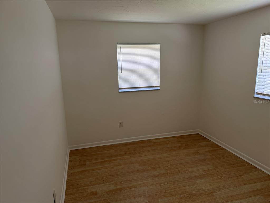 An empty bedroom with light wood-look flooring, white walls, and two windows with blinds — 2185 NW 3RD STREET, OKEECHOBEE, FL