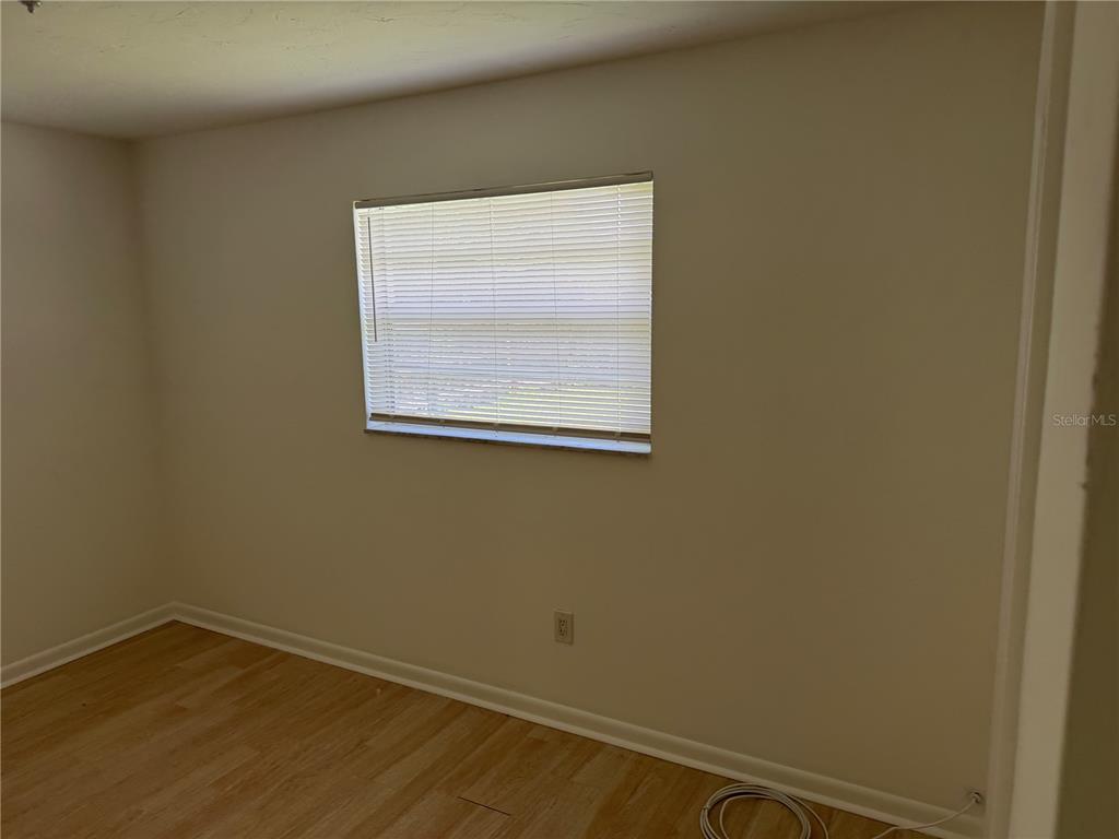 An empty room features light-colored wood-look flooring, beige walls, and a window with blinds — 2185 NW 3RD STREET, OKEECHOBEE, FL