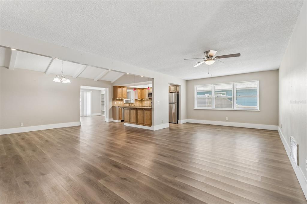 A spacious living room with light wood-look flooring flows into an open kitchen with cabinets — 13691 SERENA DRIVE, LARGO, FL