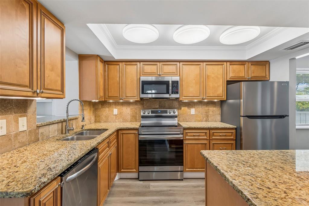 A kitchen features wood cabinets, granite countertops, stainless steel appliances, and recessed ceiling lighting — 13691 SERENA DRIVE, LARGO, FL