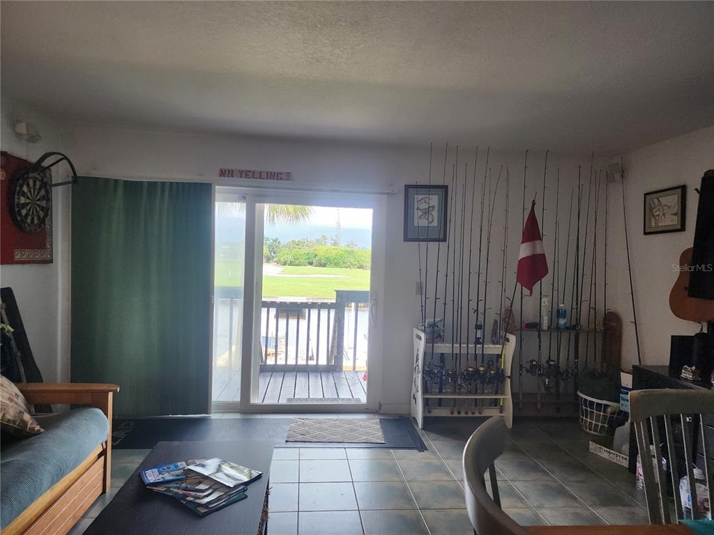 A living room features tile flooring, a sliding glass door to a deck, and fishing gear — 200 MERES BOULEVARD UNIT 19, TARPON SPRINGS, FL