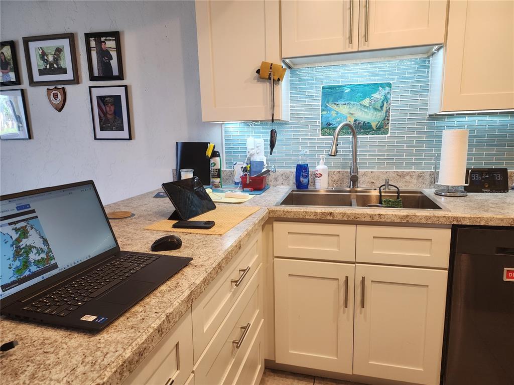 A kitchen features white cabinets, granite countertops, a stainless steel sink, and a blue backsplash — 200 MERES BOULEVARD UNIT 19, TARPON SPRINGS, FL