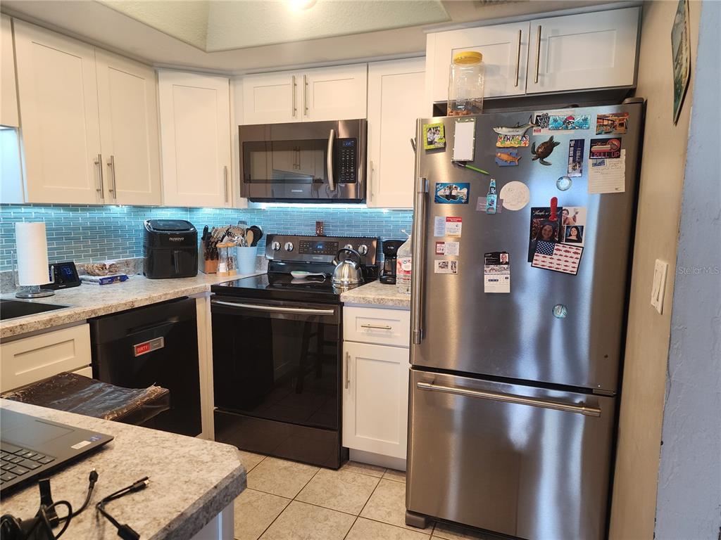 A kitchen features white cabinets, stainless steel appliances, a blue tiled backsplash, and granite countertops — 200 MERES BOULEVARD UNIT 19, TARPON SPRINGS, FL