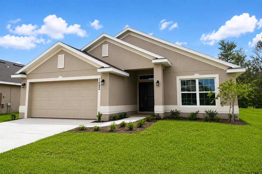 A single-story suburban house with a tan stucco exterior, a two-car garage, and a lawn — 7592 BENT TREE LOOP, ST CLOUD, FL