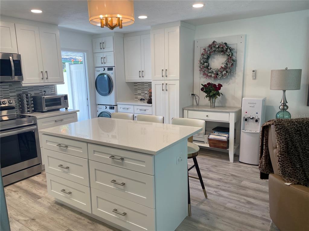 A white kitchen features a central island, stainless steel appliances, and a stacked laundry unit — 515 1ST AVENUE E, BRADENTON, FL