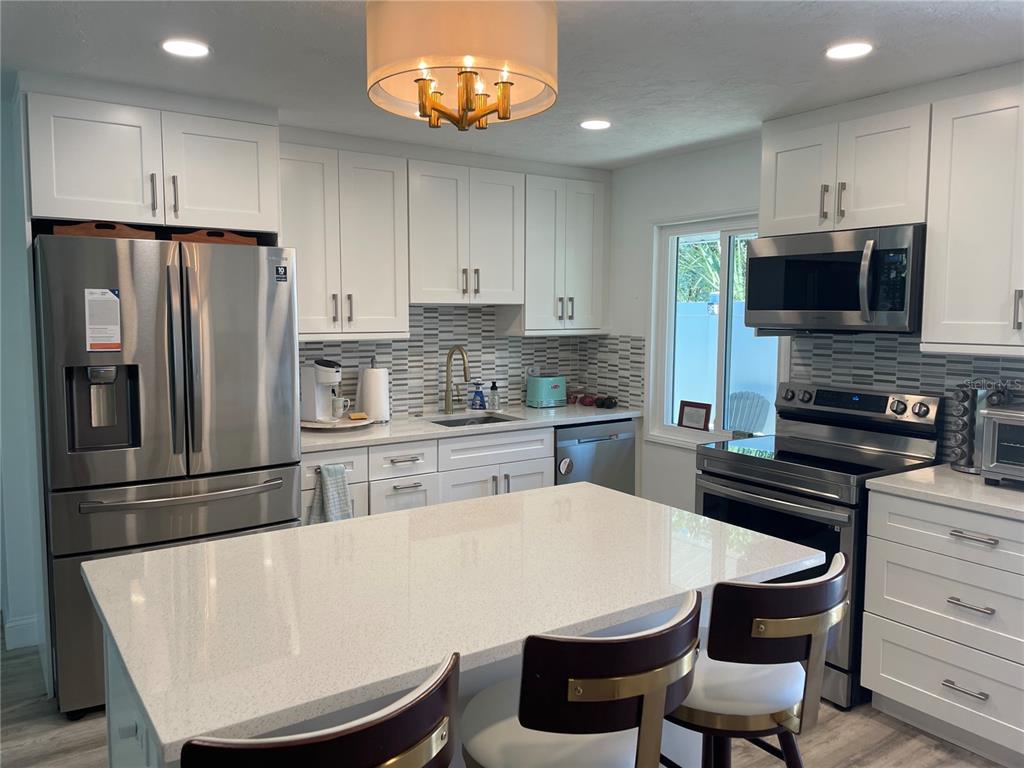 A modern kitchen features white cabinetry, stainless steel appliances, and a central quartz-topped island — 515 1ST AVENUE E, BRADENTON, FL