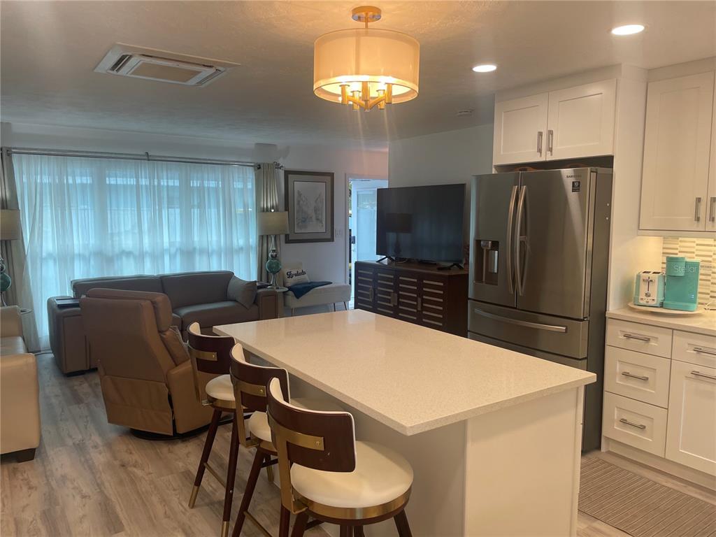 A kitchen island with bar stools sits in front of a living area with a television — 515 1ST AVENUE E, BRADENTON, FL