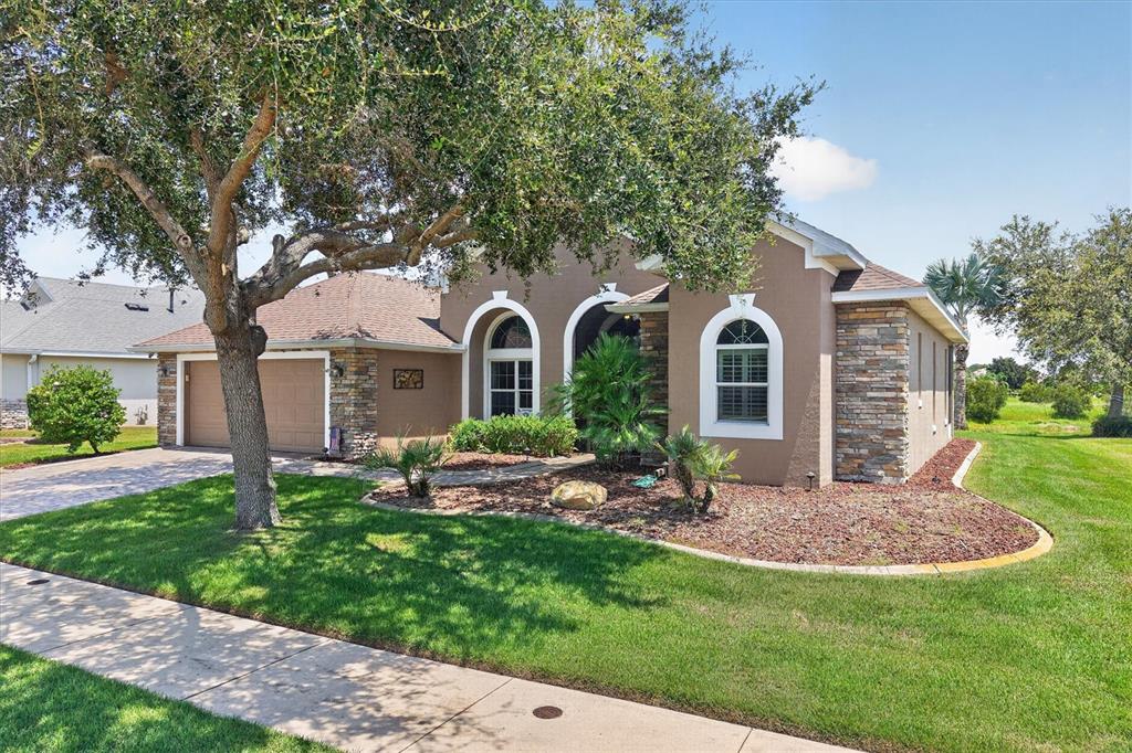 A single-story house with a tan stucco exterior, stone accents, and a two-car garage — 8920 BRIDGEPORT BAY CIRCLE, MOUNT DORA, FL