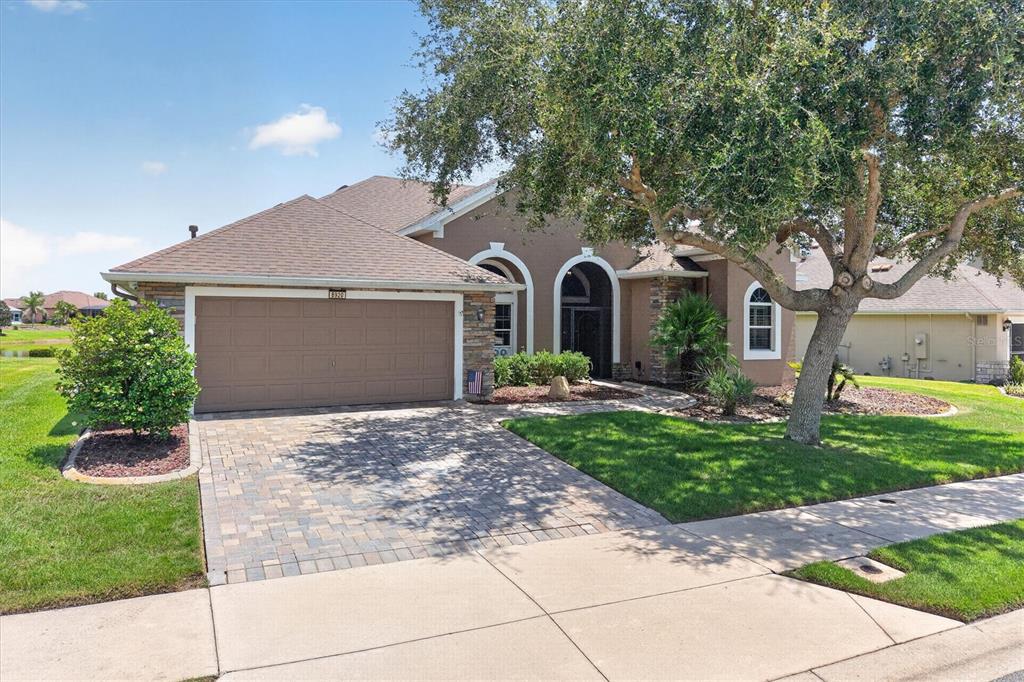 A single-story house with a brown garage, stone accents, and a large tree in front — 8920 BRIDGEPORT BAY CIRCLE, MOUNT DORA, FL