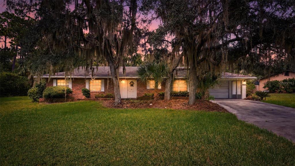 A single-story brick house with a front lawn and large trees under a sunset sky — 16529 ORANGE AVENUE, UMATILLA, FL