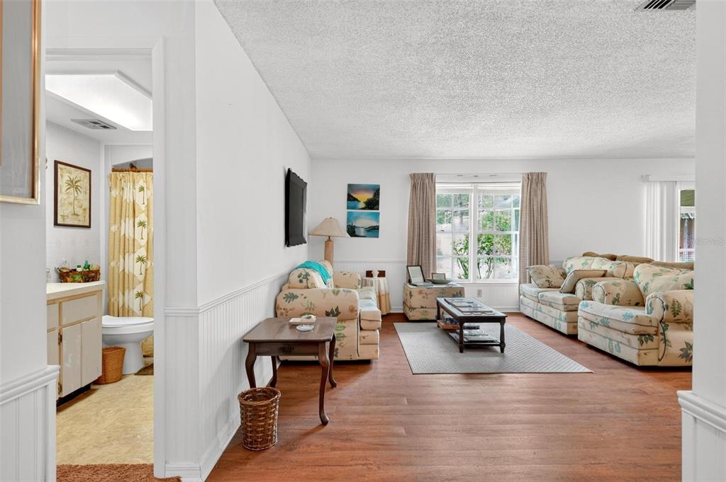 A living room with floral sofas, wood-look flooring, and an adjacent bathroom with a shower curtain — 16529 ORANGE AVENUE, UMATILLA, FL