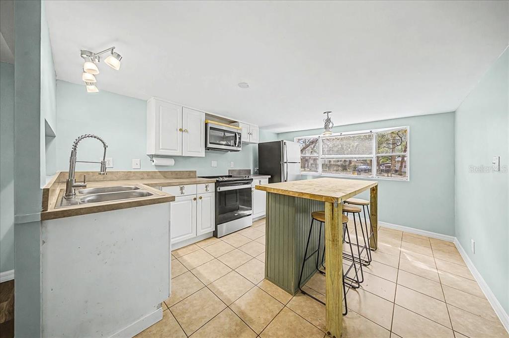 A kitchen features white cabinets, a wooden island with stools, and light-colored tile flooring — 16789 SE 8TH PLACE, SILVER SPRINGS, FL