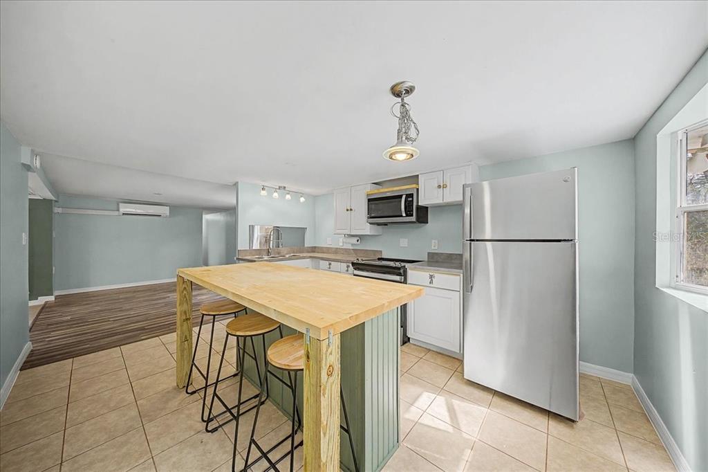 A kitchen features a wooden island with bar stools, white cabinets, and stainless steel appliances — 16789 SE 8TH PLACE, SILVER SPRINGS, FL