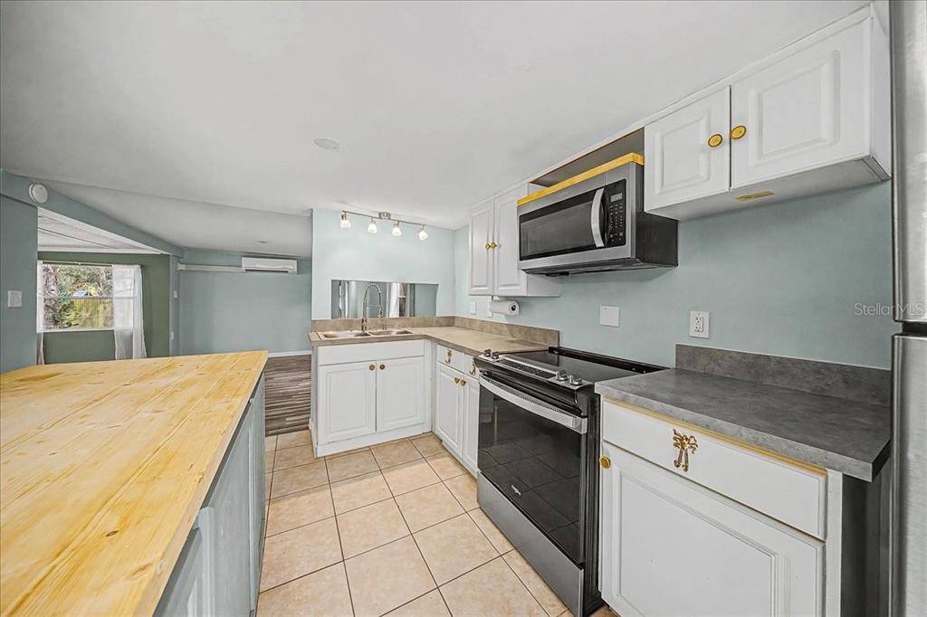 A kitchen features white cabinets, a black stove, a microwave, and a wooden countertop island — 16789 SE 8TH PLACE, SILVER SPRINGS, FL