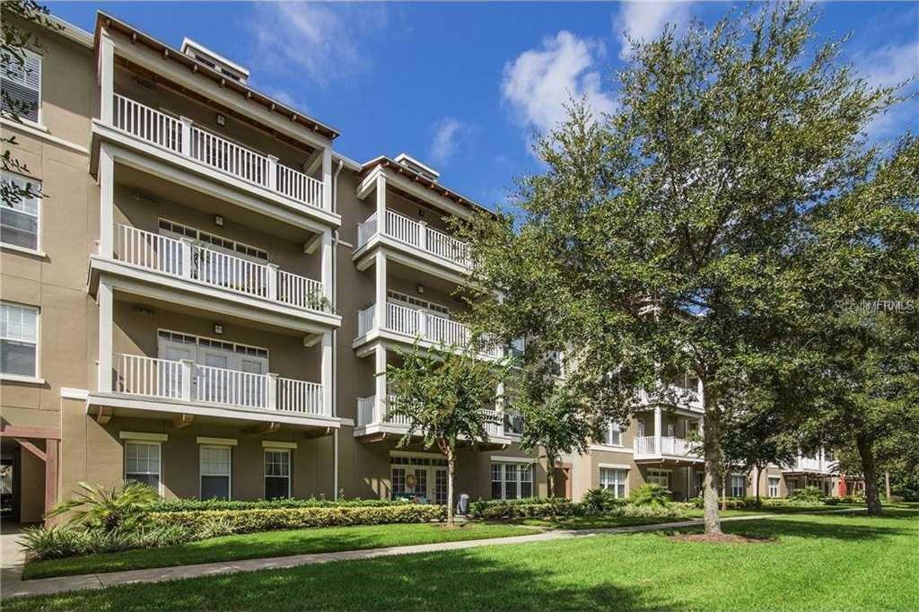 A multi-story apartment building with white balconies and a landscaped lawn under a blue sky — 1400 CELEBRATION AVE UNIT 102, CELEBRATION, FL