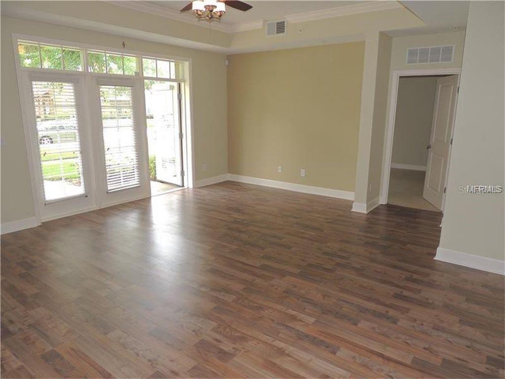 An empty room features light-colored walls, wood-look flooring, a tray ceiling, and glass doors — 1400 CELEBRATION AVE UNIT 102, CELEBRATION, FL