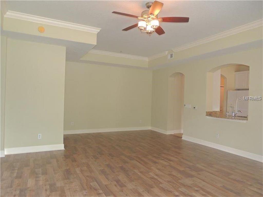 An empty living room features light green walls, wood-look flooring, and a ceiling fan — 1400 CELEBRATION AVE UNIT 102, CELEBRATION, FL