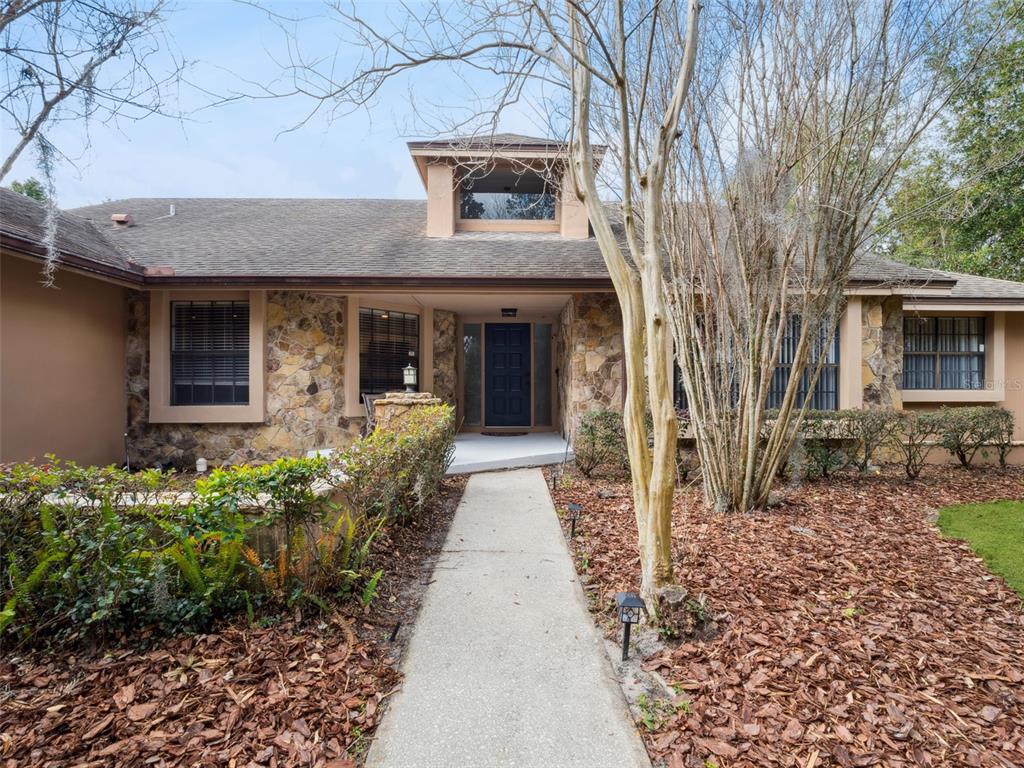 A tan single-story house with a large concrete driveway and mature trees in the yard — 5314 SHADYWOOD LANE, ORLANDO, FL