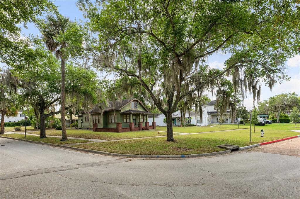 A green bungalow with a brick porch sits on a corner lot under large trees — 230 KILLARNEY DRIVE, WINTER PARK, FL