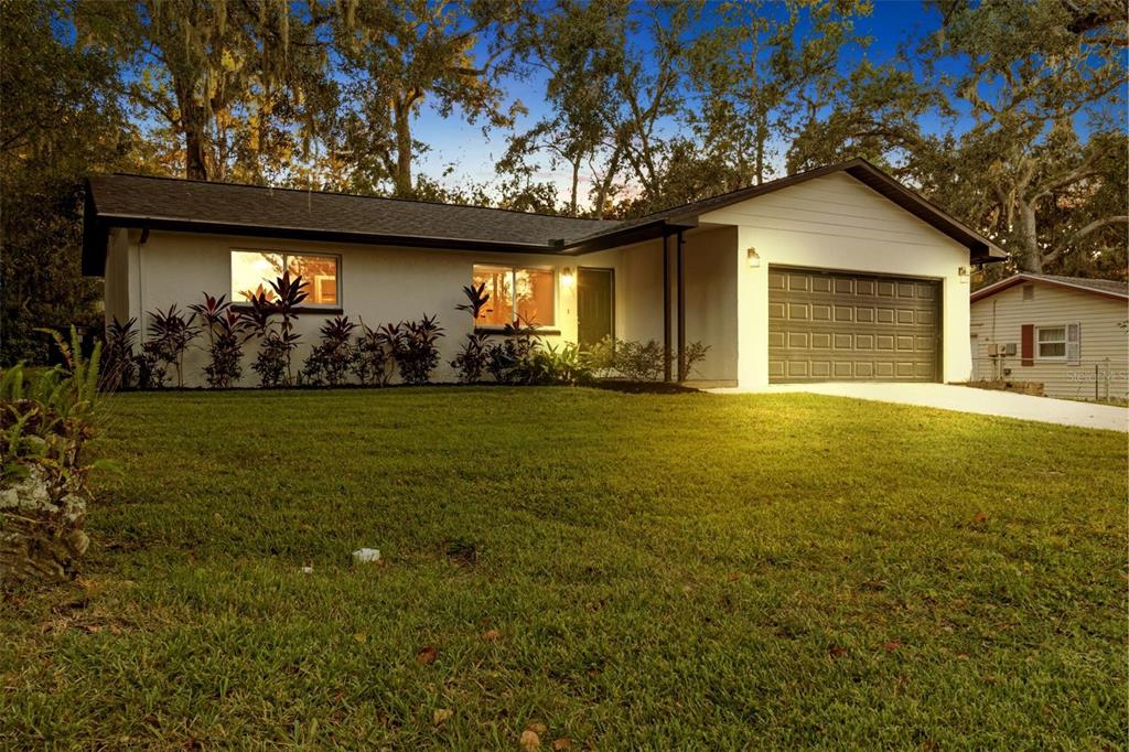 A white single-story house with a dark roof, a two-car garage, and landscaped front yard — 609 HOLLEY STREET, BROOKSVILLE, FL