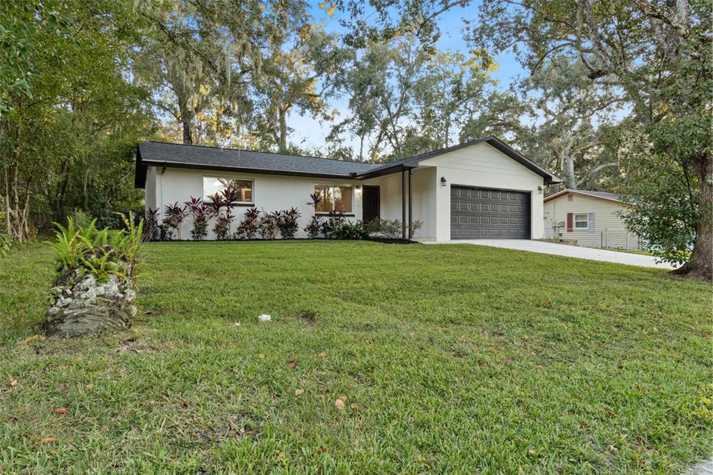 A single-story house with a white exterior, dark roof, and attached garage sits on a lawn — 609 HOLLEY STREET, BROOKSVILLE, FL