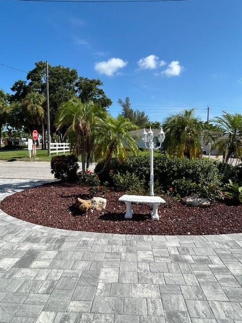 A white bench and lamp post sit in a landscaped garden with red mulch — 9312 KINGSTON ROAD, BRADENTON, FL