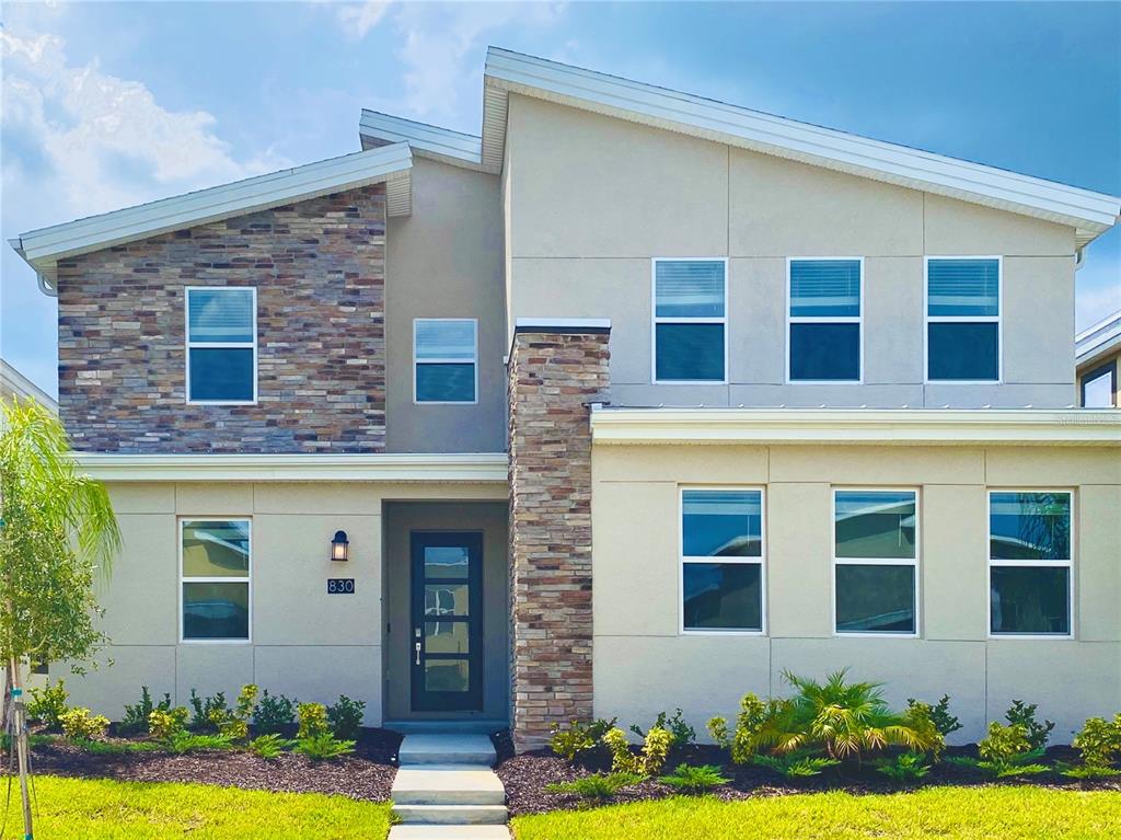 A two-story house exterior features a stone veneer facade, stucco walls, and a modern entryway — 830 DROP SHOT DRIVE, DAVENPORT, FL