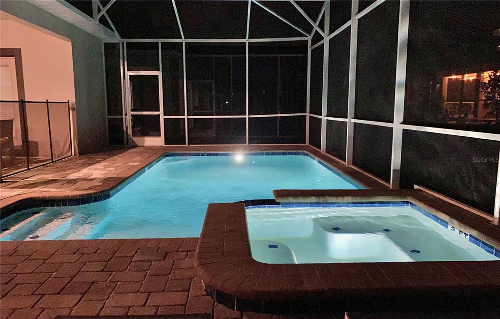 A swimming pool and attached spa are enclosed within a screened-in lanai at night — 830 DROP SHOT DRIVE, DAVENPORT, FL