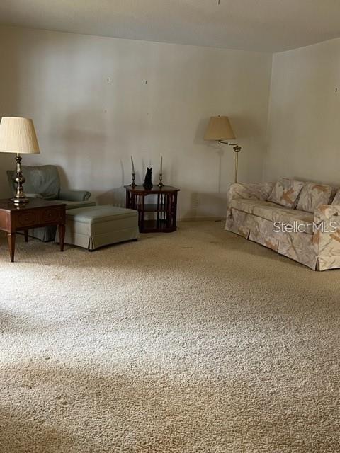A living room features beige carpeting, a patterned sofa, an armchair with an ottoman, and lamps — 627 MIDWAY DRIVE UNIT B, OCALA, FL