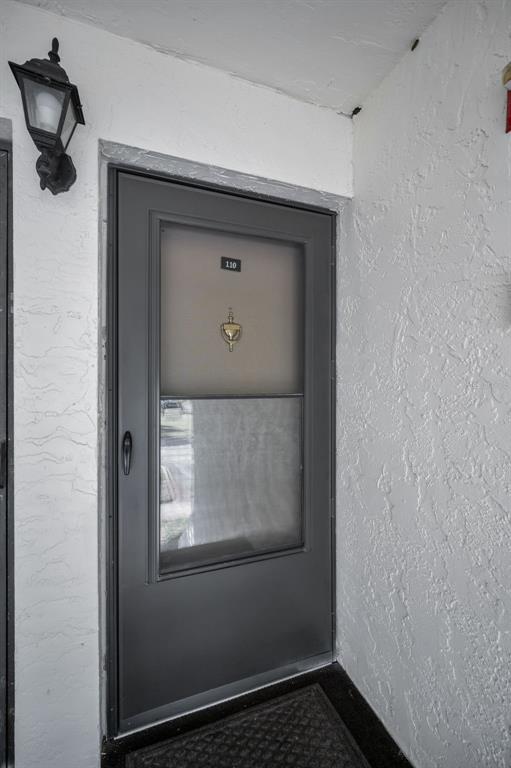 A dark gray storm door with a brass knocker and number 110 is mounted on a white exterior wall — 110 CYPRESS CT UNIT 3-82, OLDSMAR, FL