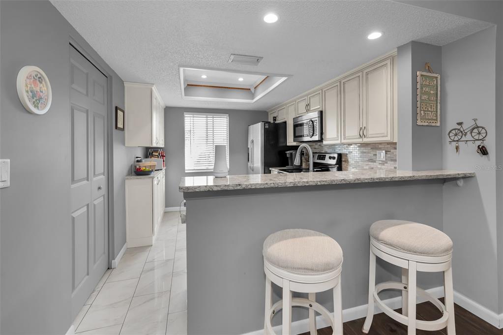 A kitchen features white cabinetry, granite countertops, a breakfast bar with stools, and tile flooring — 110 CYPRESS CT UNIT 3-82, OLDSMAR, FL